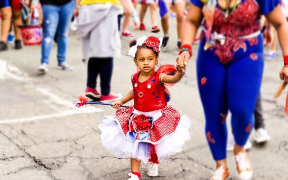 Young girl holding mother's hand dressed in red, white and blue at Caribbean Carnival 2017.