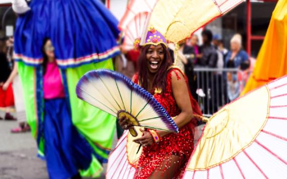 Woman smiling, dressed in bright carnival costume during 2017 Caribbean Carnival procession.