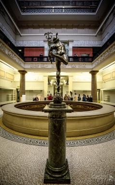 Hermes statue overlooking circular balcony where last visitors are having a tour.