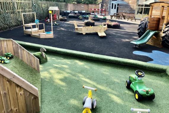 Kinder Hubs outdoor play area with soft grass area and wooden climbing sculptures