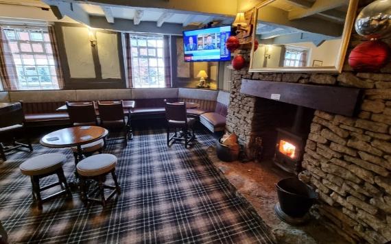 A view of a seating area inside The Old Vic pub with a log burner fireplace and sports on a TV