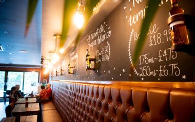 A seating bench under a chalkboard wall and warm coloured lights inside Bar Pintxos