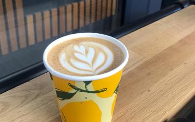 A brightly coloured cup filled with coffee with a flower latte art design