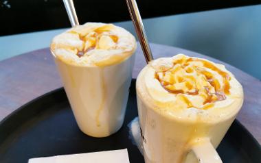 A close up of two latte's with a caramel drizzle on top of whipped cream from Caffé Nero