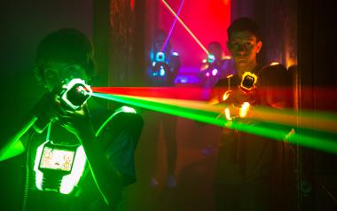 A boy with a green laser gun faces the camera in an action pose with team mates behind him