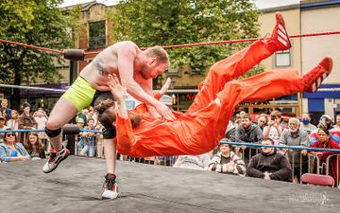 A wrestler throwing another wrestler in an orange jump suit in a wrestling ring on the Flag Market