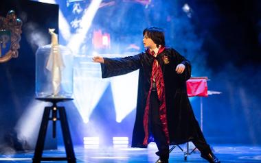 A boy in wizard costume on a stage performing magic