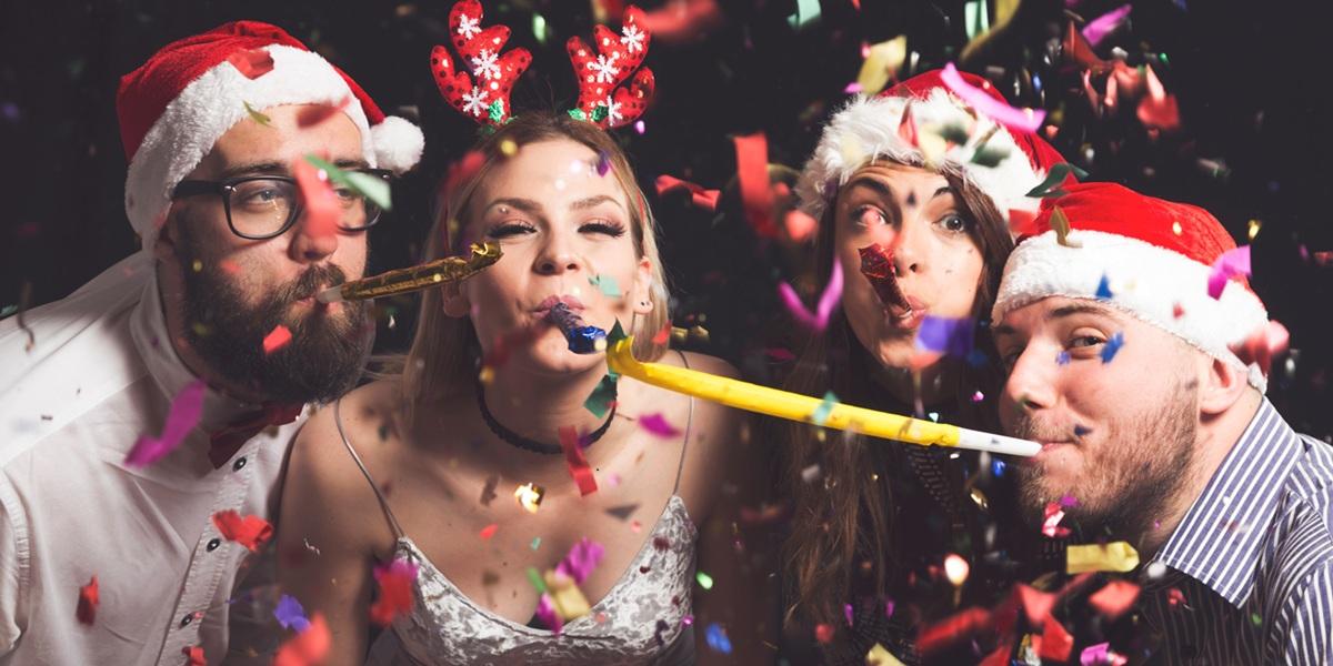 Two beautiful young couples having fun at New Year's party, dancing and blowing party whistles.