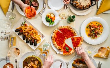 A table with a plate of oysters, a plate of pizza and people sharing drinks 