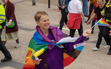 A woman wearing a rainbow flag over her shoulders waving a smaller rainbow pride flag