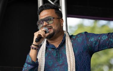 A man on a stage with blue robes and big sunglasses singing into a microphone. Photo by Karen Browne.