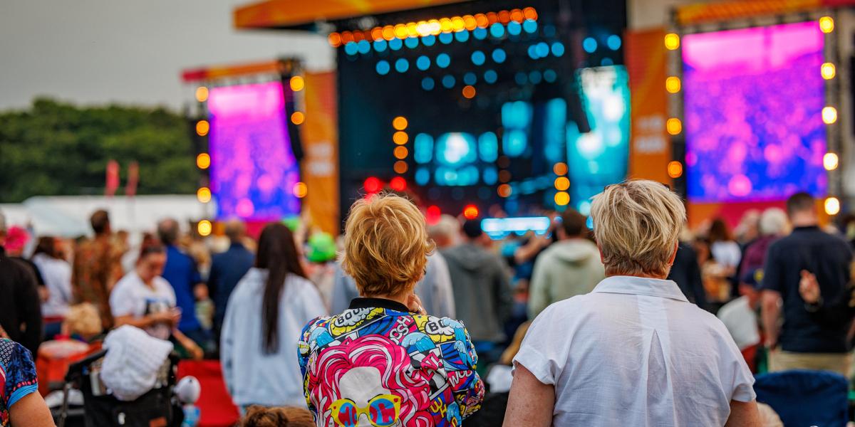 Two people watching a band perform on a stage in the distance