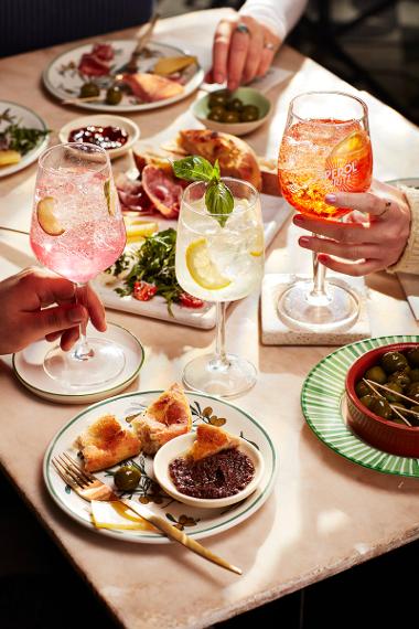 A close up of a table of light bite meals and peoples hands holding drinks