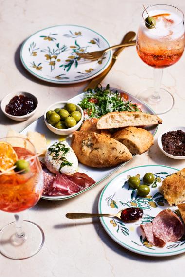 A plate of poached egg, bread, deli meats and olives with sprits drinks