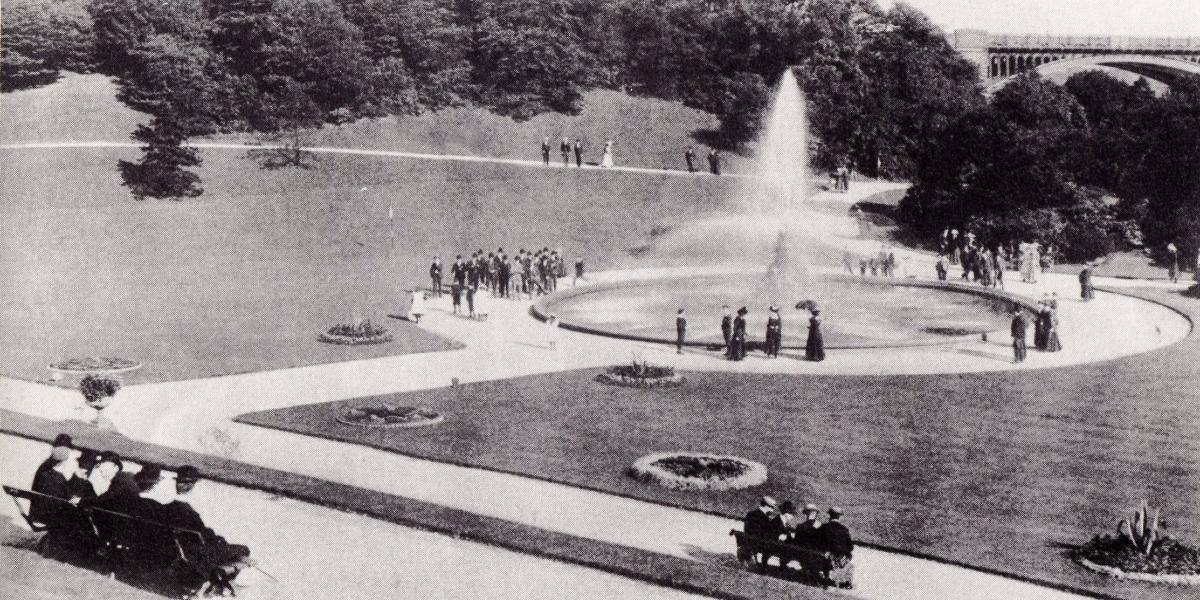 Vintage black and white photograph of men and women wearing Victorian attire relaxing around the fountain in Miller Park.