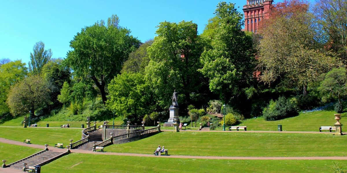 View of Miller Park's higher pathways from afar, with Earl of Derby Statue, green space, and trees.