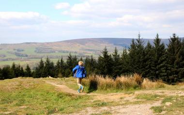 Young boy running along path at summit of Beacon Fell with hills and trees in the background.