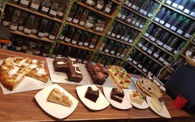 Assortment of cakes on counter with jars of tea on shelves behind.