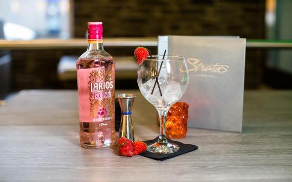 Gin, strawberries, and glass arranged on table in front of Stratos menu.