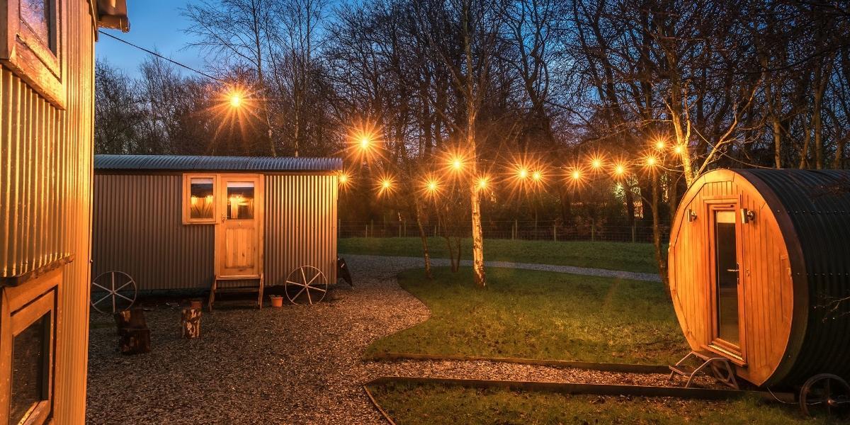 Samlesbury Hall's shepherd huts lit up at night with string lights.