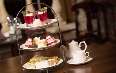 Three tier afternoon tea next to teapot on table inside The Walled Garden.