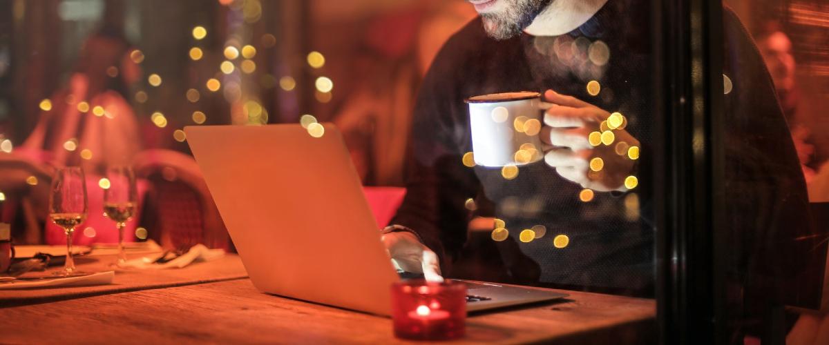 Man sipping coffee and browsing on laptop inside café. 